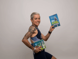 Séverine Guérif posant en tenue d’équipe de France, tenant dans chaque main ses deux premiers livres « 2x Championne du Monde » et « 1 cancer, 3x Championne du Monde », posture dynamique évoquant la course.